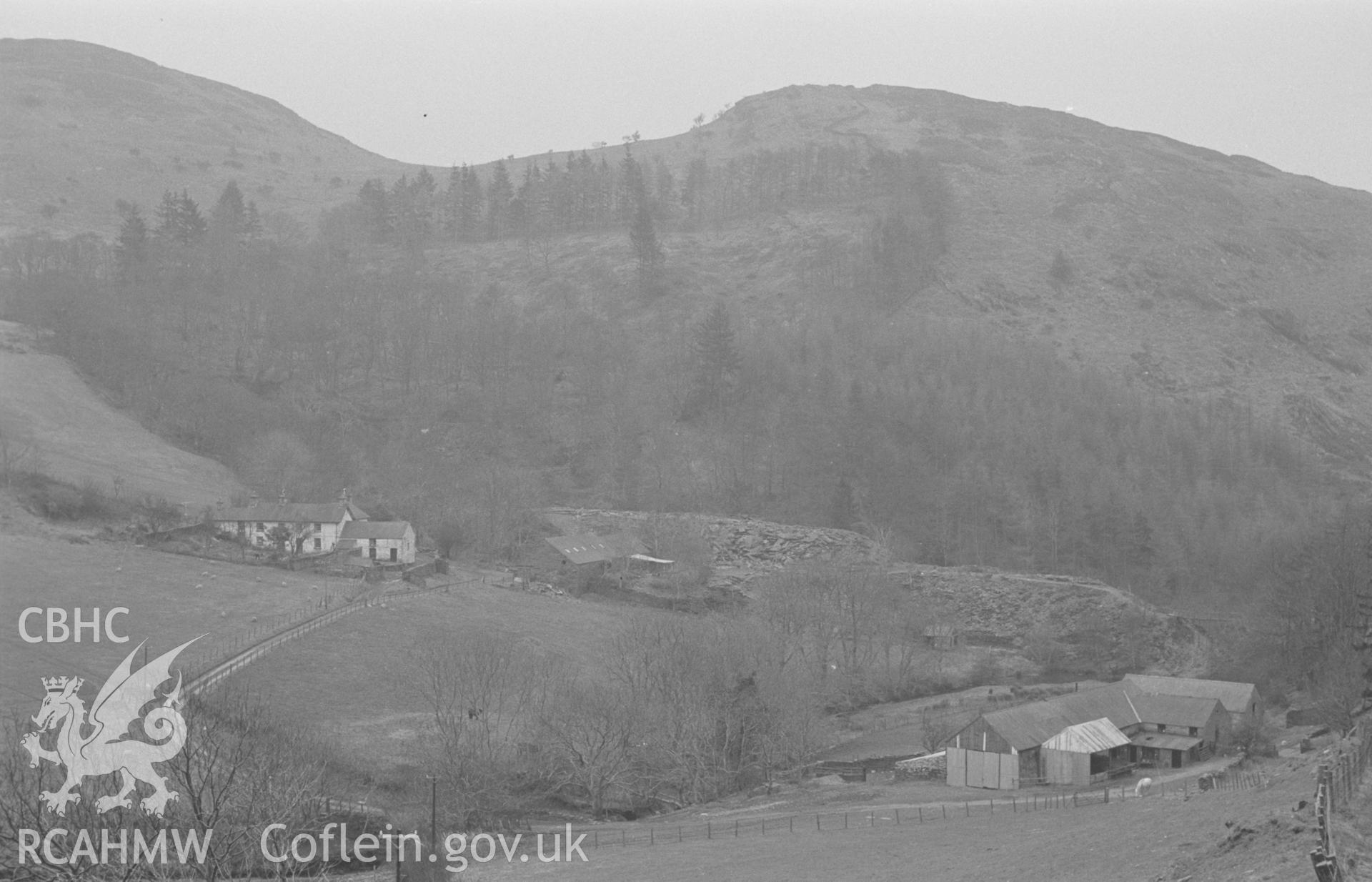 Digital copy of a black and white negative showing Cymerau Farm and Cardigan Slate Works with Foel Fawr behind, Eglwysfach, Machynlleth. Photographed in March 1964 by Arthur O. Chater from Grid Reference SN 6992 9629, looking south south west.