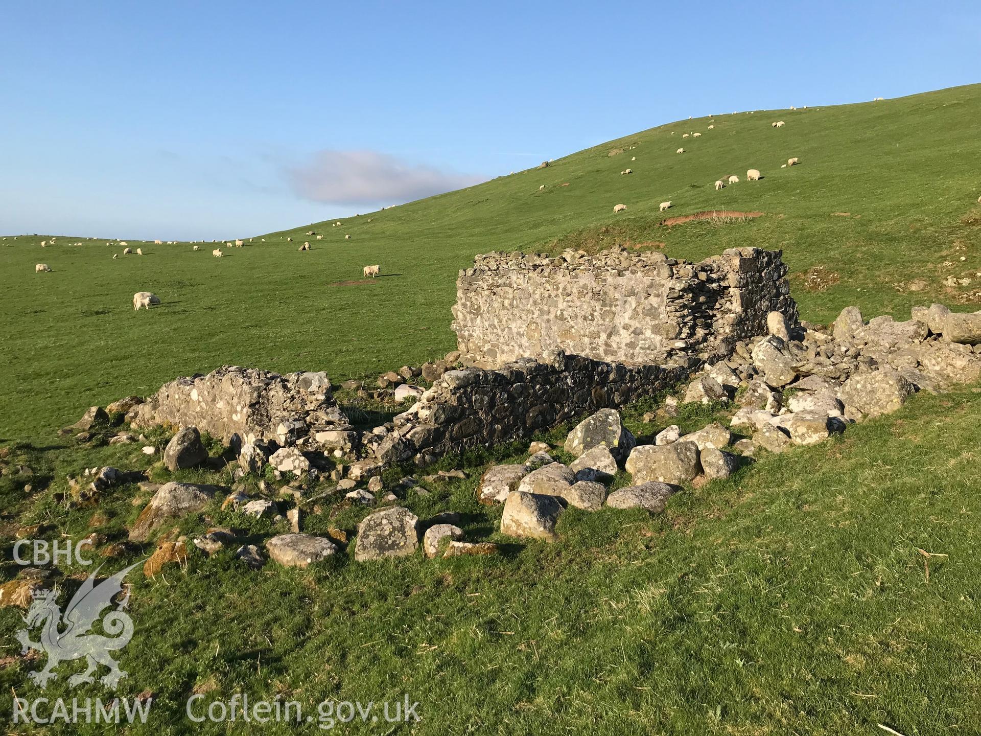 Colour photo of ruined 2 roomed building 600m west of Bod Silin house, presumably a field barn. The stonework suggests no great age. Since used as a dump for larger boulders gathered from surrounding fields (SH 666 727), taken by Paul R. Davis 19/4/2018.