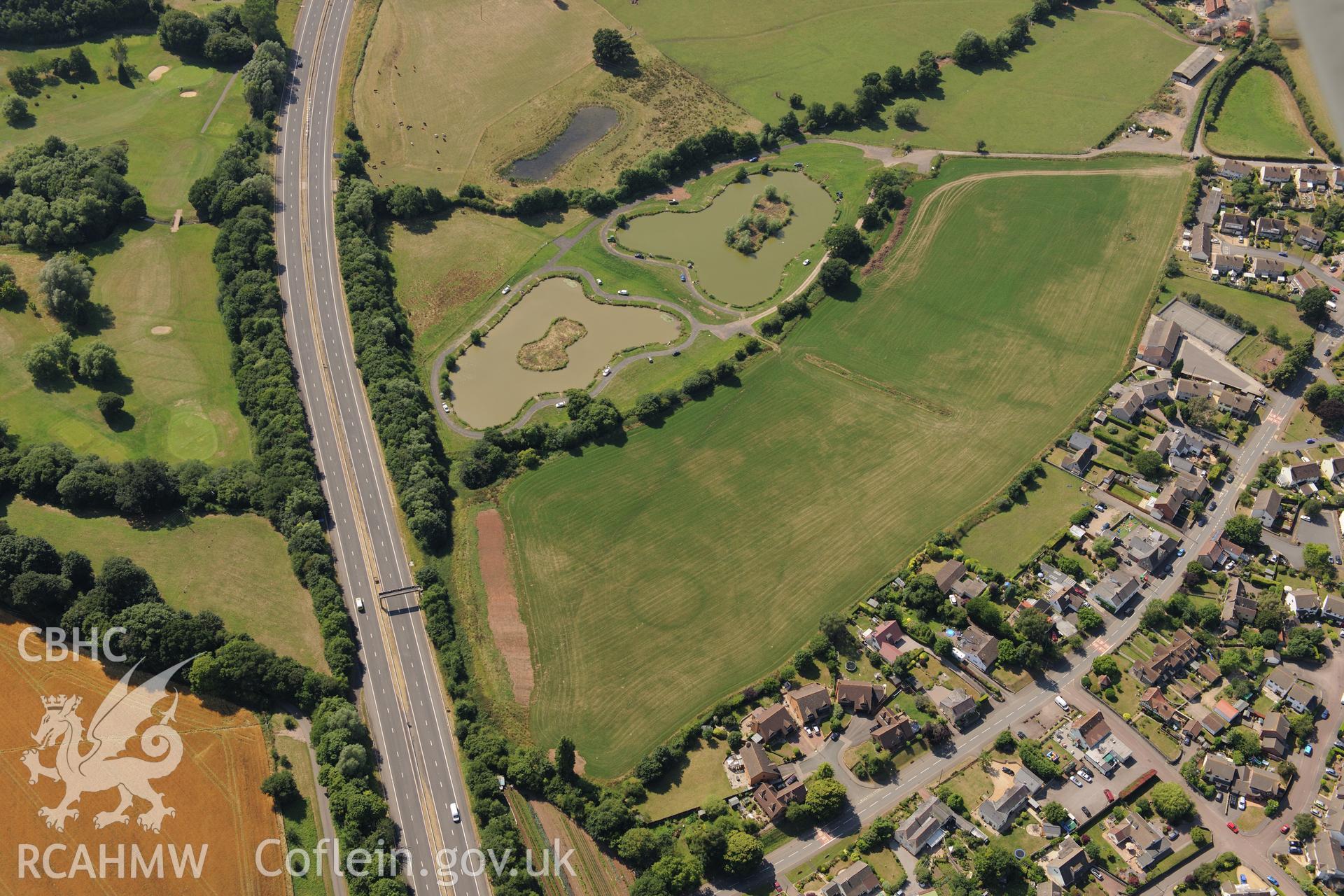 Round barrow cropmarks and the village of Newton Green,south west of Chepstow, with the M48 passing to the south. Oblique aerial photograph taken during the Royal Commission?s programme of archaeological aerial reconnaissance by Toby Driver on 1st August