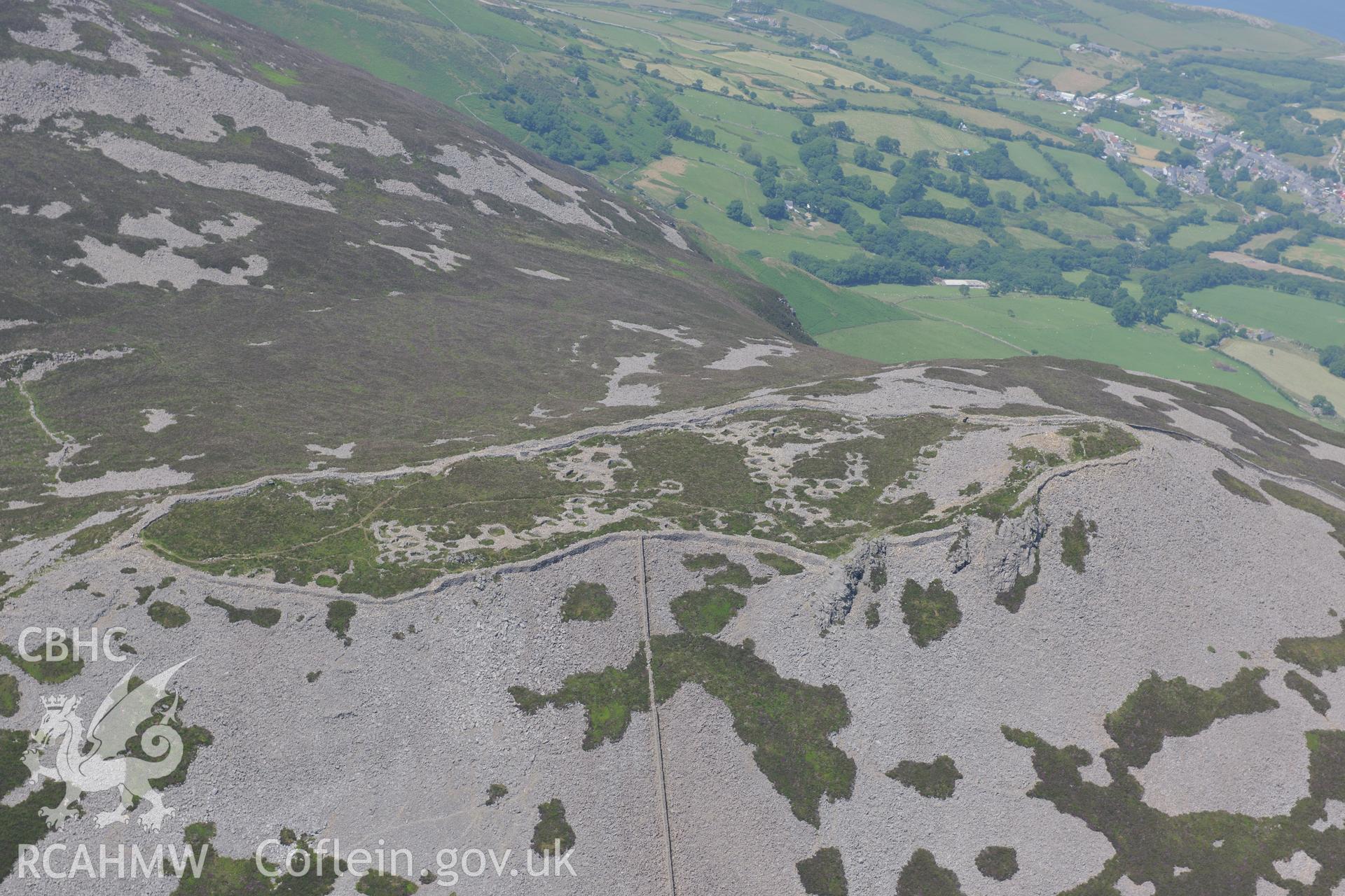 Tre'r Ceiri hillfort with the village of Trefor beyond, on the Lleyn Peninsula. Oblique aerial photograph taken during the Royal Commission?s programme of archaeological aerial reconnaissance by Toby Driver on 12th July 2013.