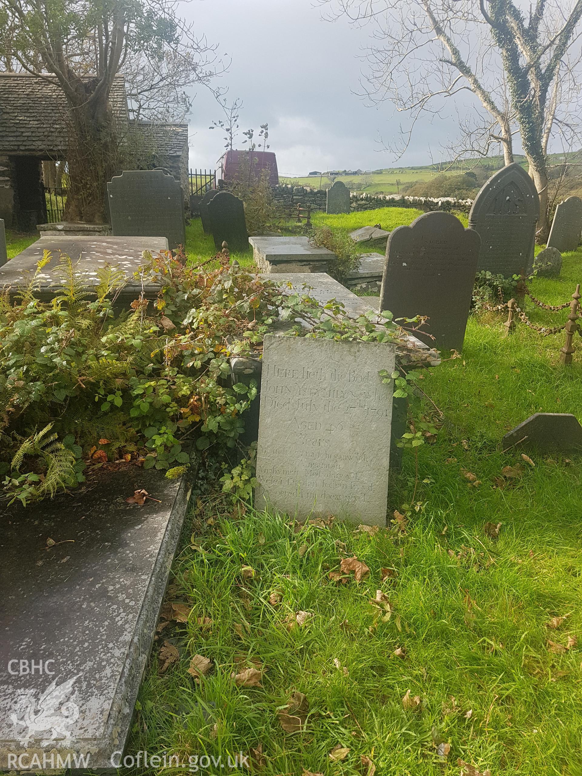 View of the gravestone of John Ystumllyn in its context at St Cynhaearn's churchyard. Photographed by Helen Rowe of RCAHMW on 10th October 2020.