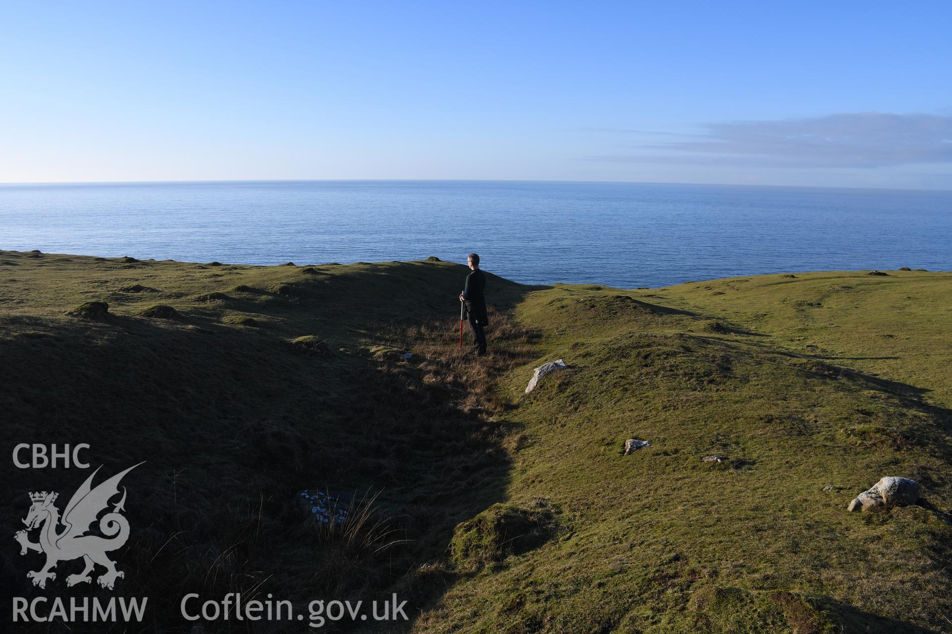 N end of inner ramparts showing gate  with figure for scale. Camera facing N. From photographic survey of Castell Bach promontory fort (NPRN 93914) using 1m scales and human figures. Undertaken by Hannah Genders Boyd for CHERISH project condition monitoring 13/01/2022.
Produced with EU funds through the Ireland Wales Co-operation Programme 2014-2020. All material made freely available through the Open Government Licence.