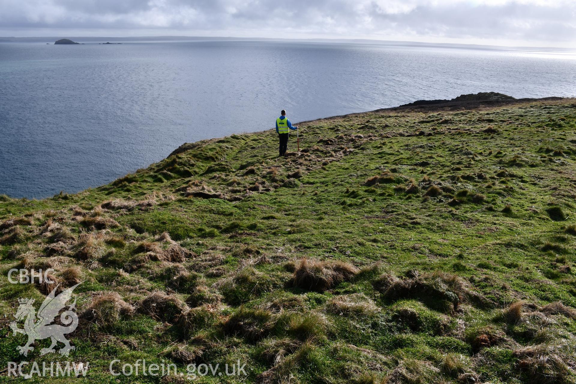 Reinstatement of turf over trench from Autumn 2021 excavation. Camera facing south. Person and 1m scale. Taken by Hannah Genders Boyd. Produced with EU funds through the Ireland Wales Co-operation Programme 2014-2023. All material made freely available th