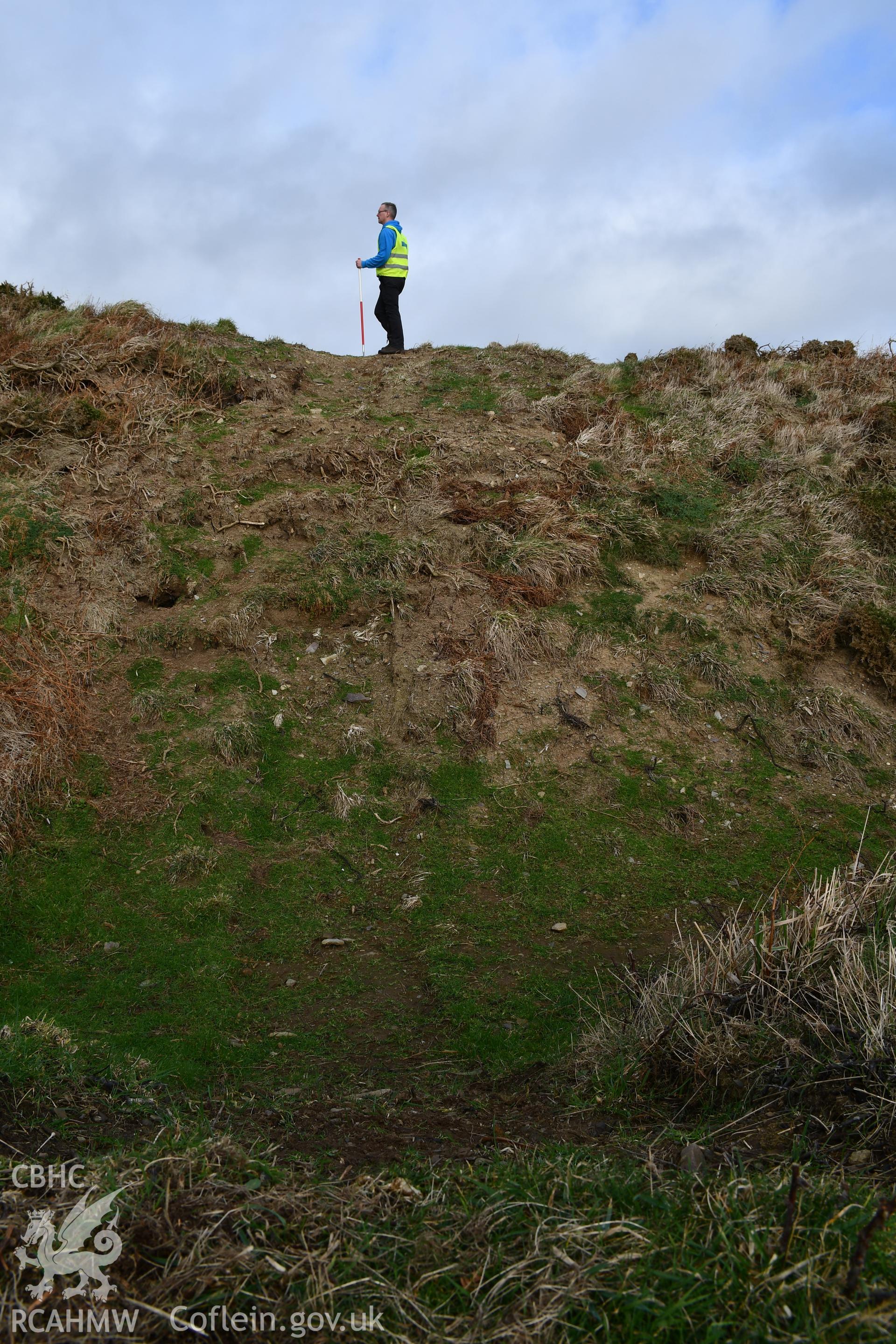 Reinstatement of turf over trench through rampart and ditch from Autumn 2021 excavation. Camera facing N. Person and 1m scale. Taken by Hannah Genders Boyd. Produced with EU funds through the Ireland Wales Co-operation Programme 2014-2023. All material ma