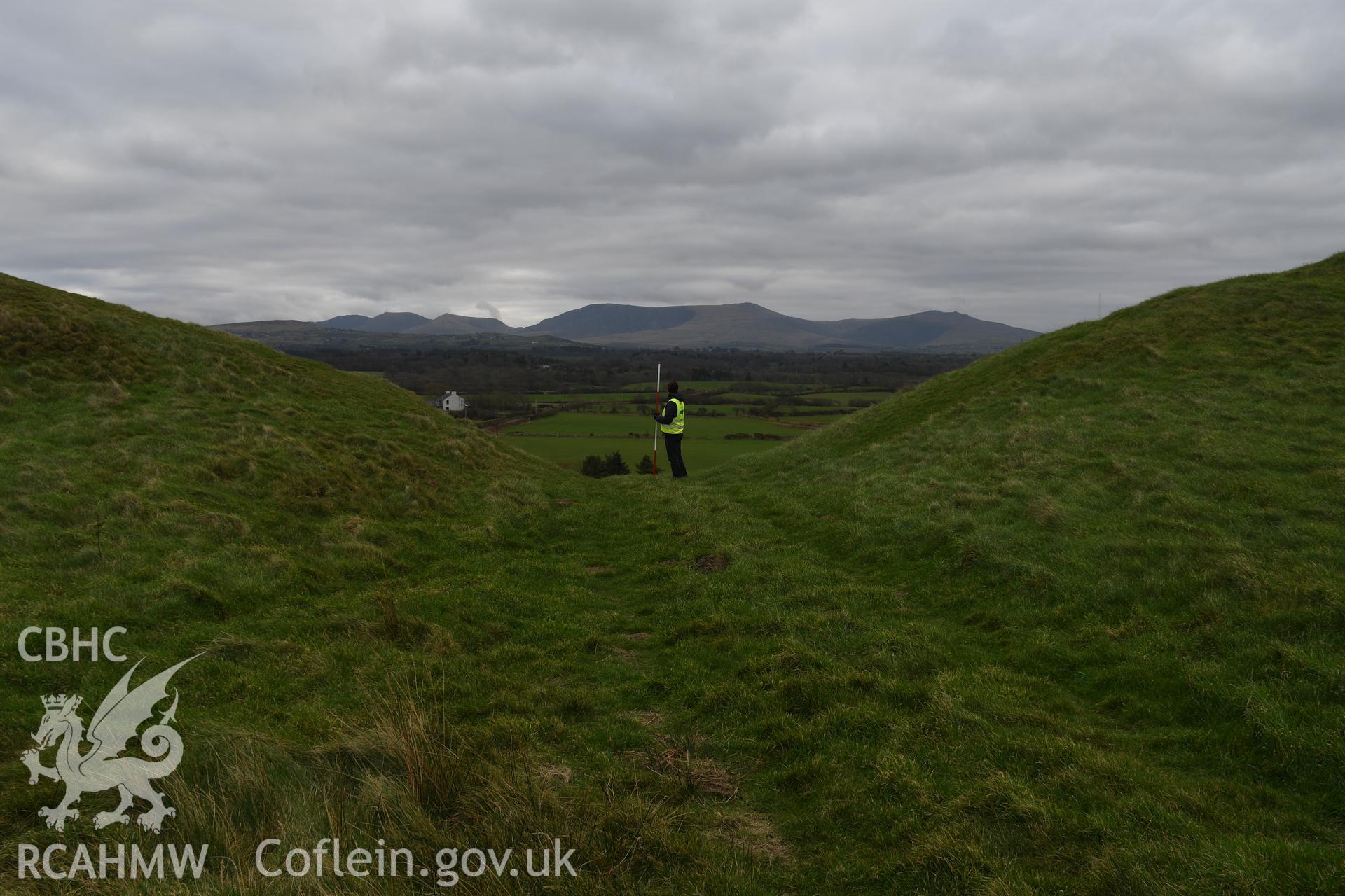 Entranceway to hillfort enclosure, figure and 2m scale. Taken by Hannah Genders Boyd. Produced with EU funds through the Ireland Wales Co-operation Programme 2014-2023. All material made freely available through the Open Government Licence.