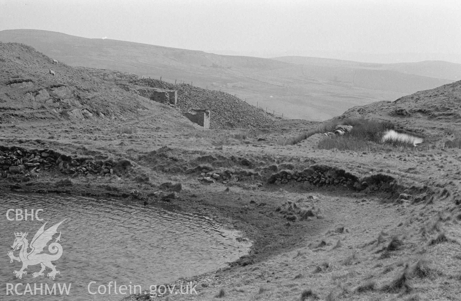 Digital copy of a black and white negative showing Glog-Fawr leadmine; the dam end of the reservoir and mine buildings. Photographed by Arthur Chater on 14 April 1968. Looking south east from Grid Reference SN 749 708.