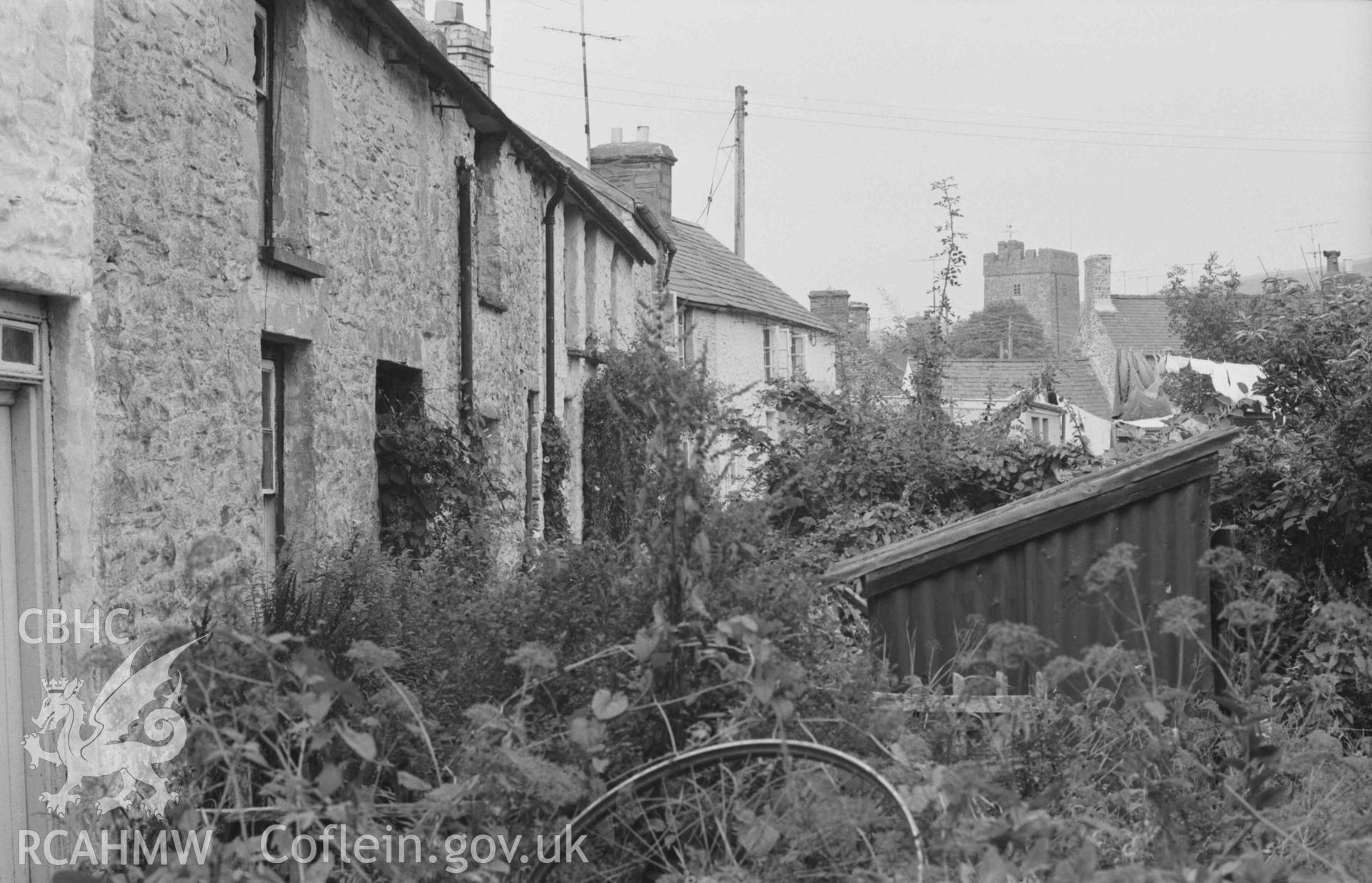 Digital copy of a black and white negative showing view looking along the backs of the houses facing the river in Doldre; church tower in background. Photographed by Arthur Chater on 29 August 1968. Looking north east from Grid Reference SN 678 595.