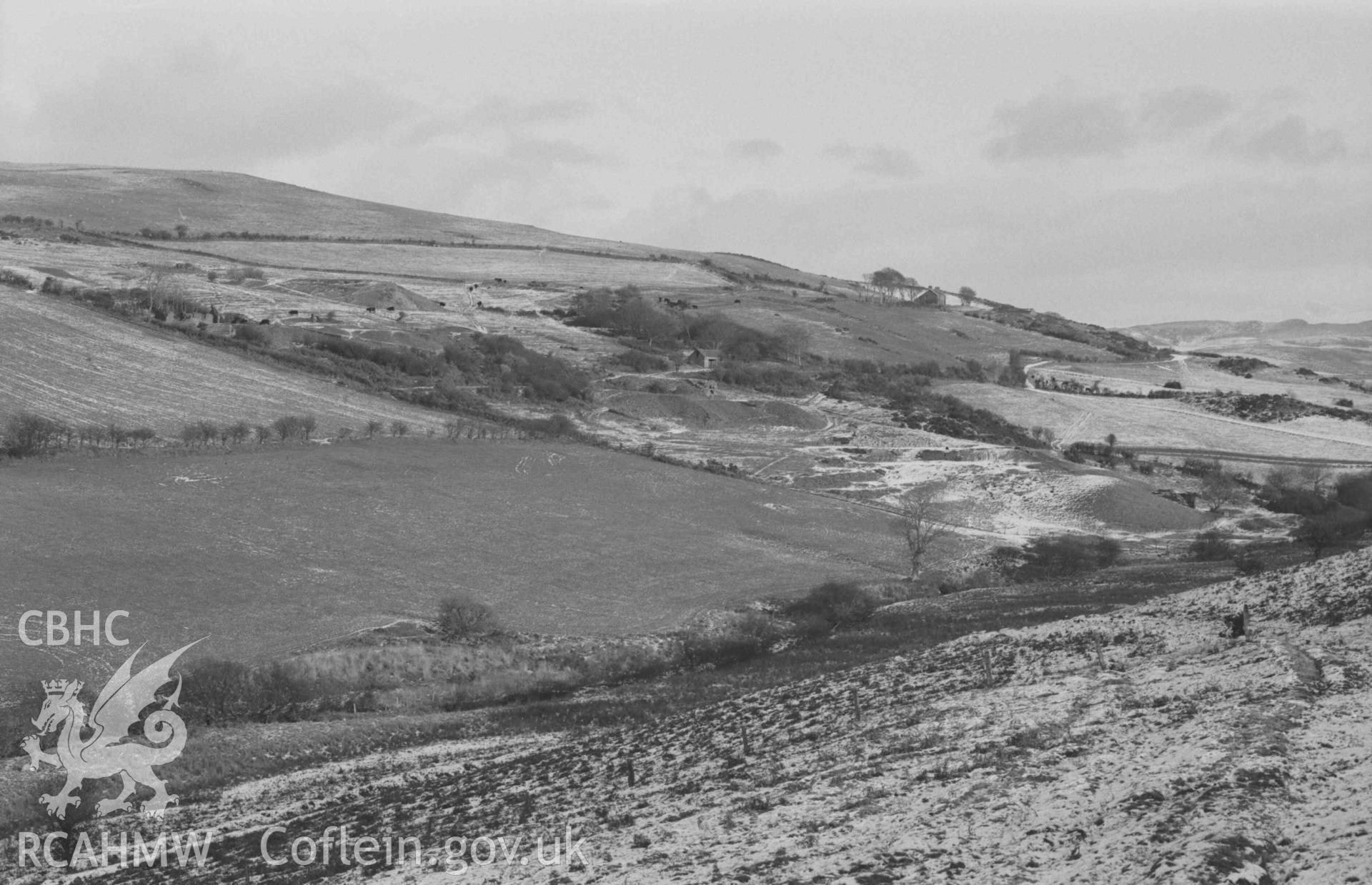 Digital copy of a black and white negative showing Mynydd-Gorddu mine, with the farm in the distance, from the track on the south side of the valley. Photographed by Arthur Chater on 29 December 1968. Looking east north east from Grid Reference SN 664 858.