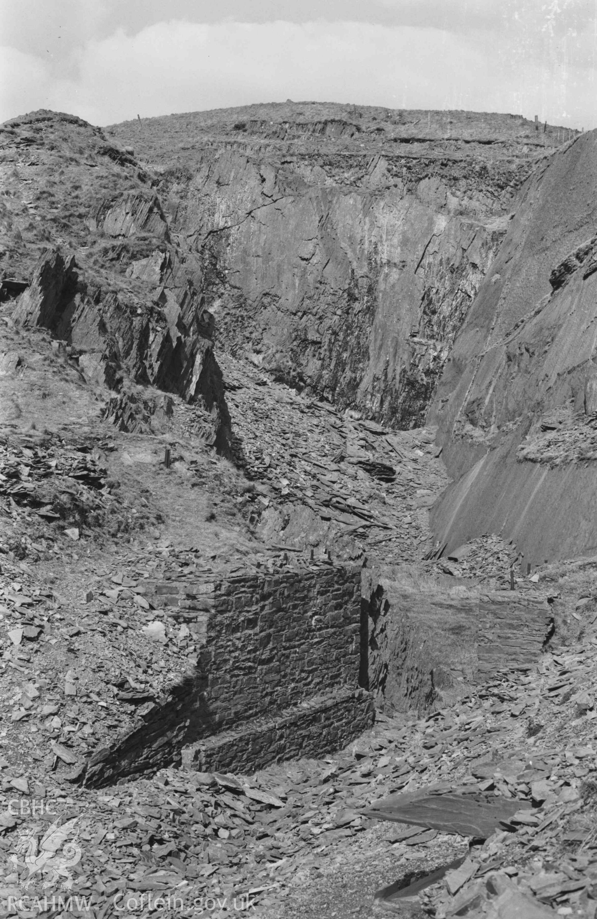 Digital copy of a black and white negative showing view looking into the quarry behind Ffynnon-Cadno, showing walls lining entrance. Photographed by Arthur Chater on 2 April 1969. Looking north north east from Grid Reference SN 7403 8082.