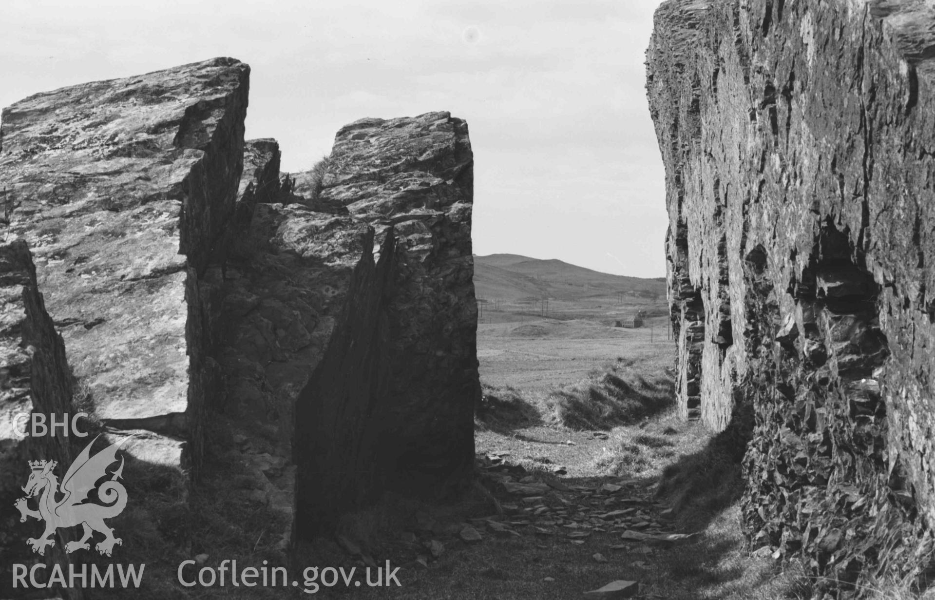 Digital copy of a black and white negative showing rock cutting of acqueduct on hillside 100m north of Ffynnon-Cadno; Llywernog leadmine ruins in distance. Photographed by Arthur Chater on 2 April 1969. Looking west from Grid Reference SN 7409 8071.