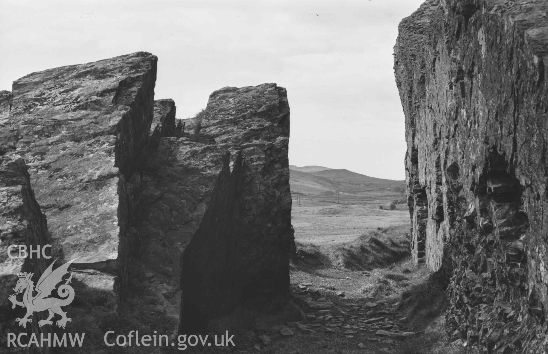 Digital copy of a black and white negative showing rock cutting of acqueduct on hillside 100m north of Ffynnon-Cadno; Llywernog leadmine ruins in distance. Photographed by Arthur Chater on 2 April 1969. Looking west from Grid Reference SN 7409 8071.