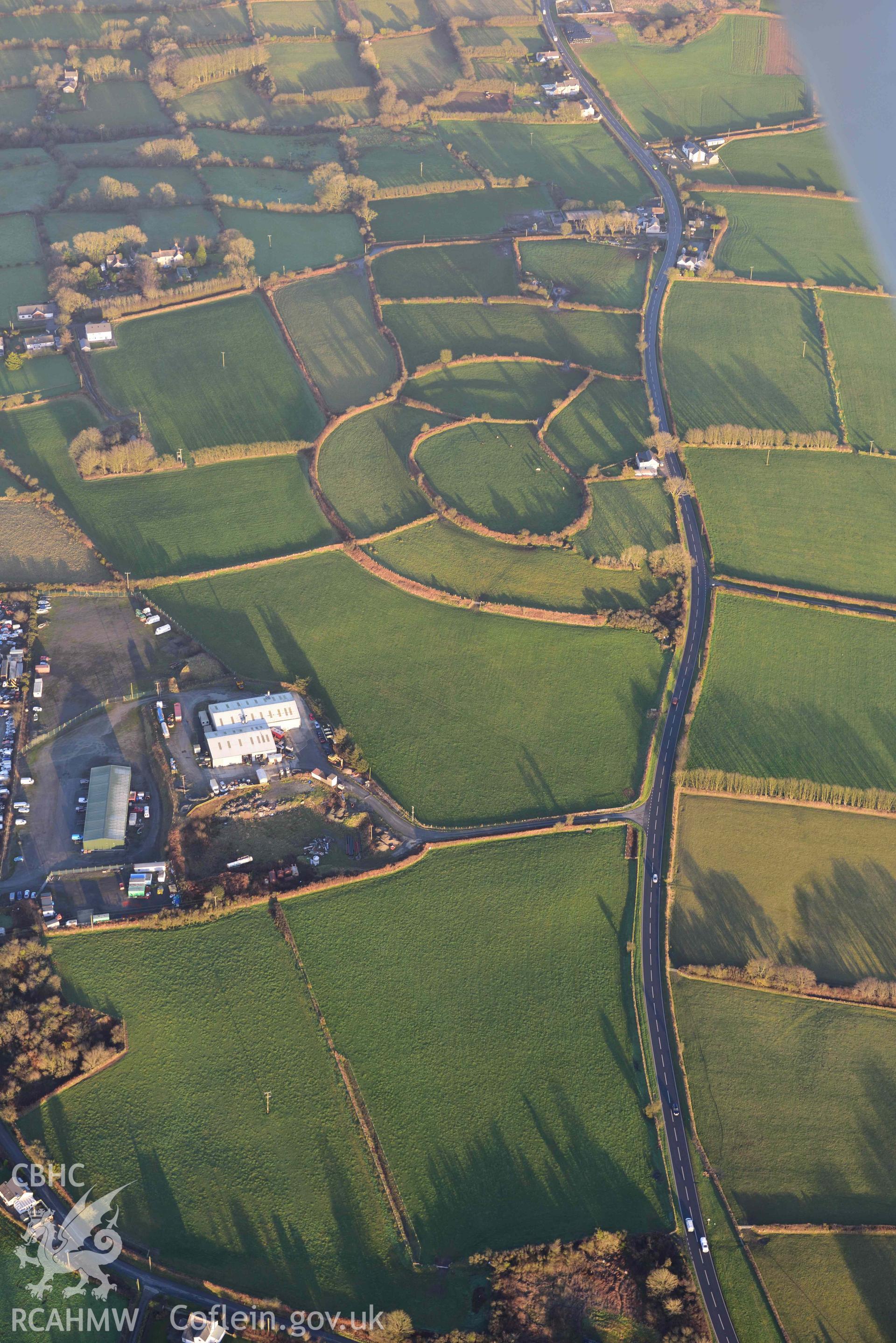 Oblique aerial photograph of Castell Nadolig hillfort, view from west in low winter light. Taken during the Royal Commission