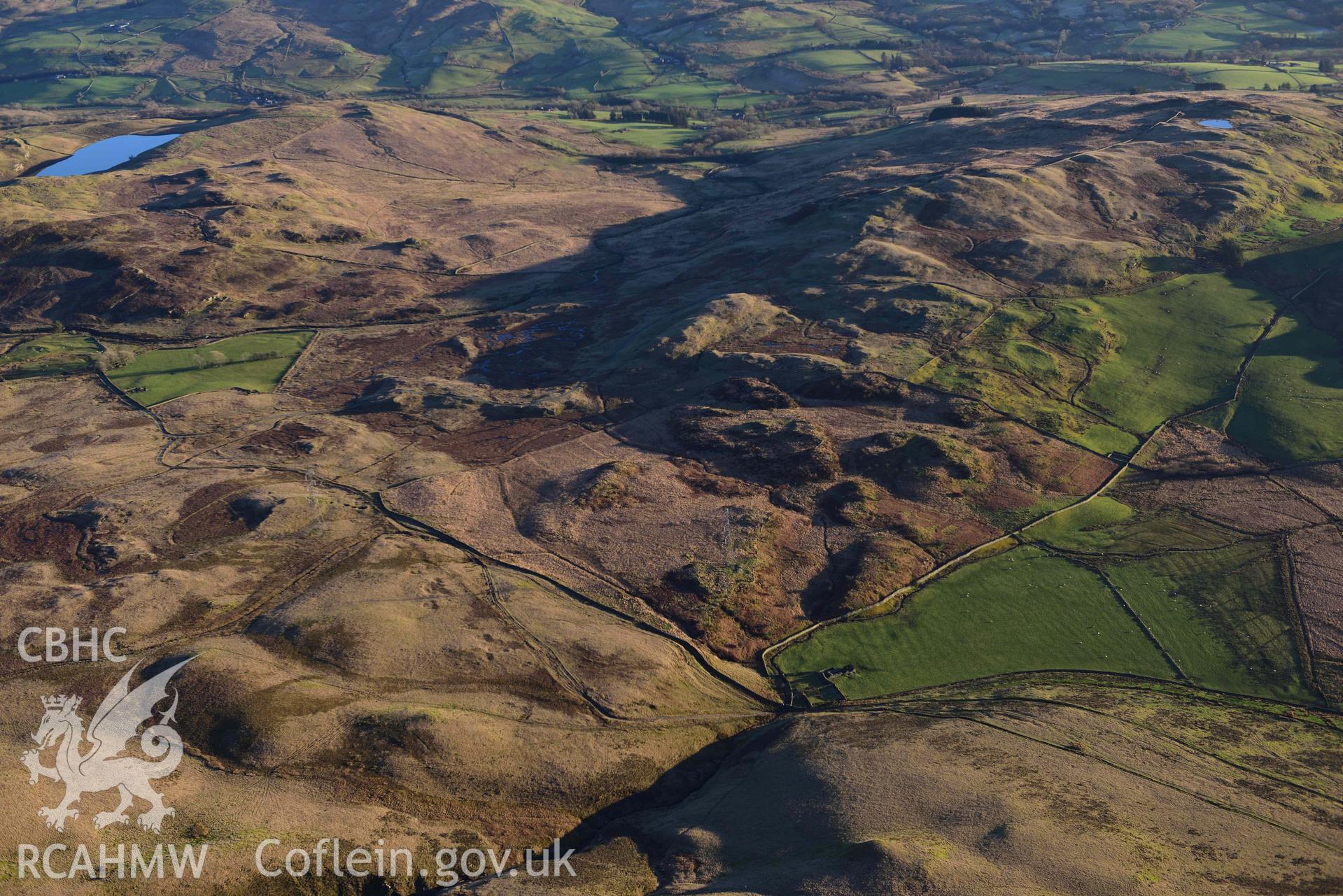 Oblique aerial photograph showing wide landscape view from the north of Dolbelydr enclosed hut group. Taken during the Royal Commission’s programme of archaeological aerial reconnaissance by Toby Driver on 17th January 2022