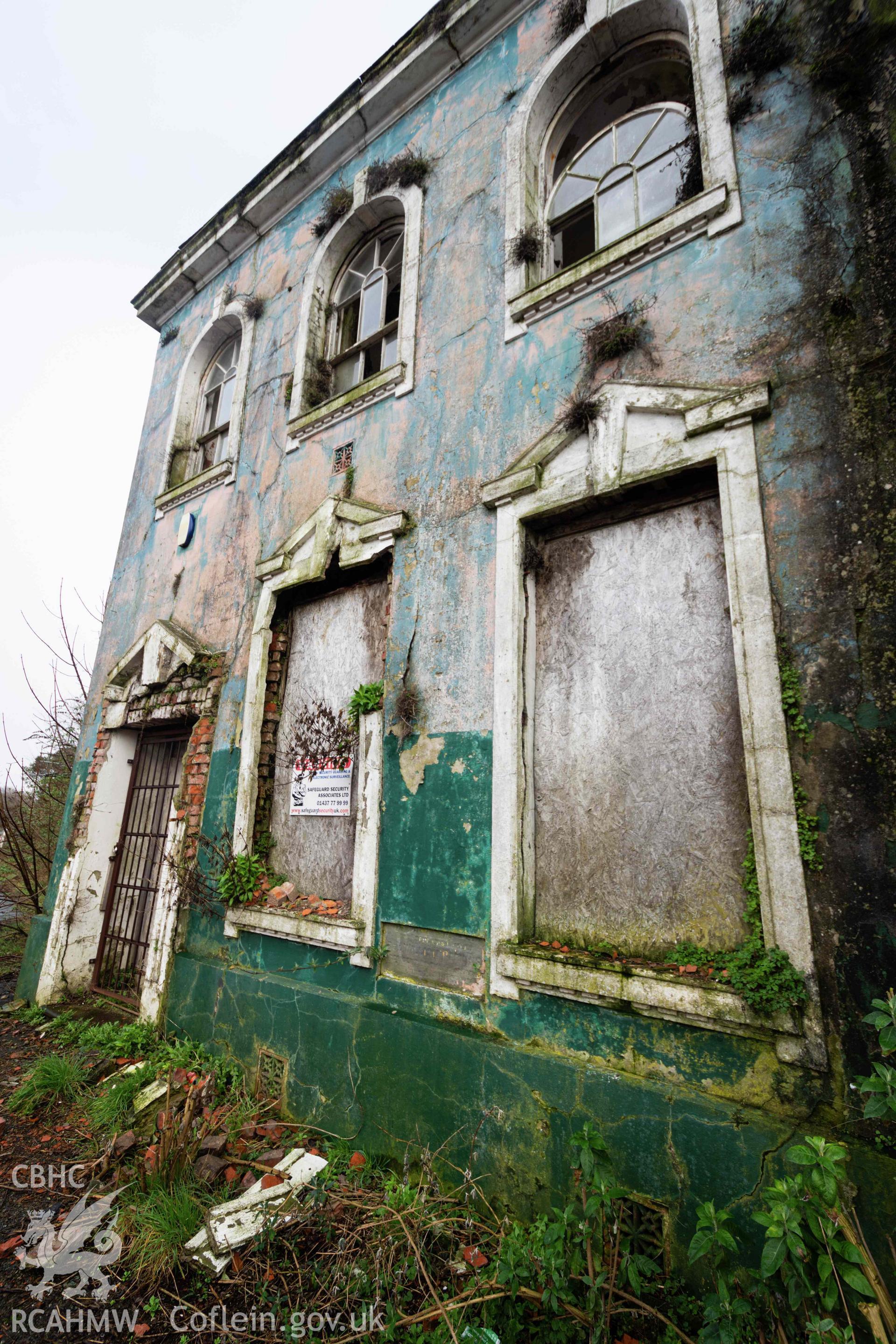 Boarded windows and closed off doorway. West façade. Overgrown and derelict. Perrots Road Wesleyan Methodist Chapel, Haverfordwest. Part of a photographic survey conducted by Meilyr Powel on 20 February 2023.