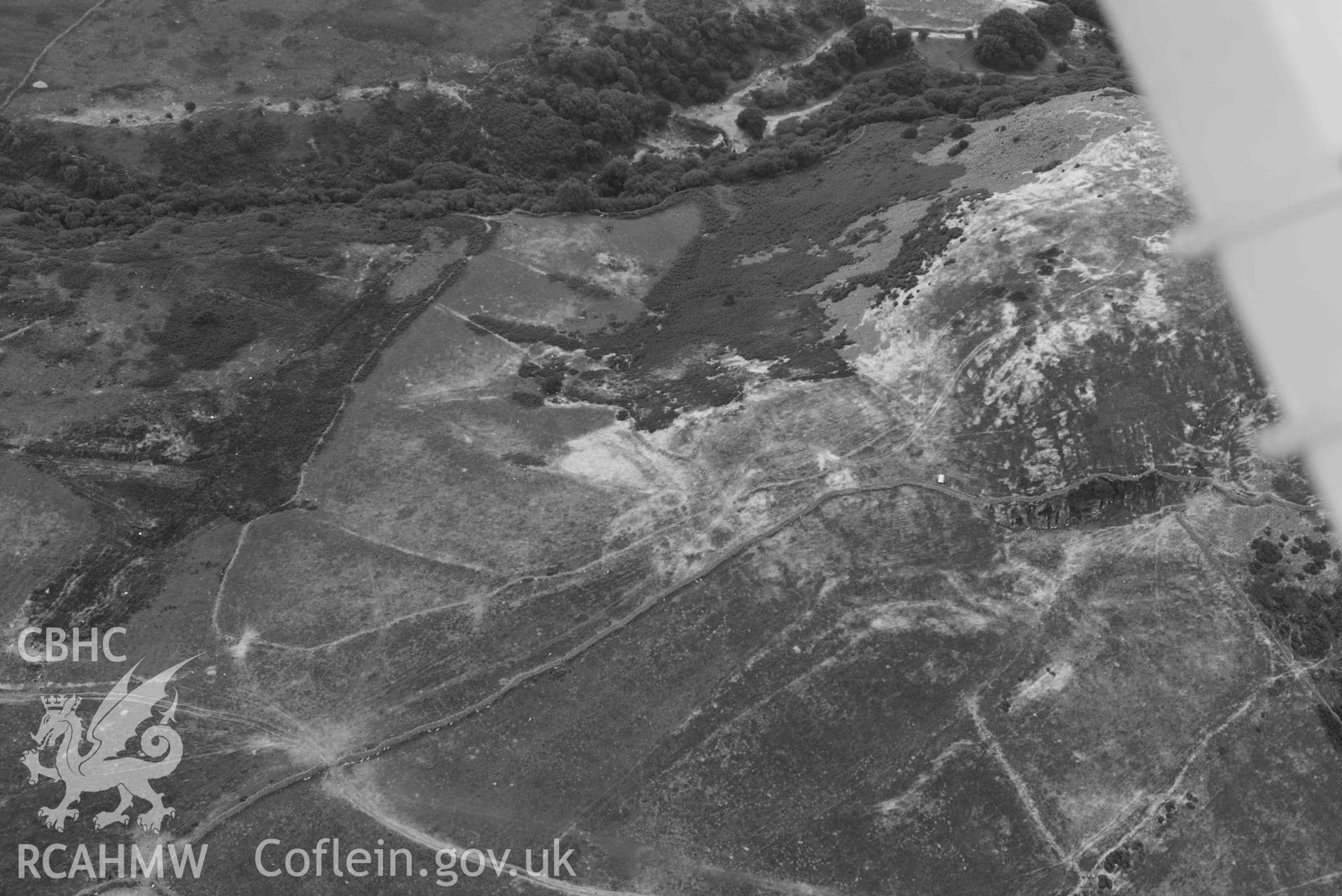 Dinas Llanfairfechan and hut circles near Dinas. Oblique black and white aerial photograph taken during the Royal Commission’s programme of archaeological aerial reconnaissance by Toby Driver on 10 July 2018.