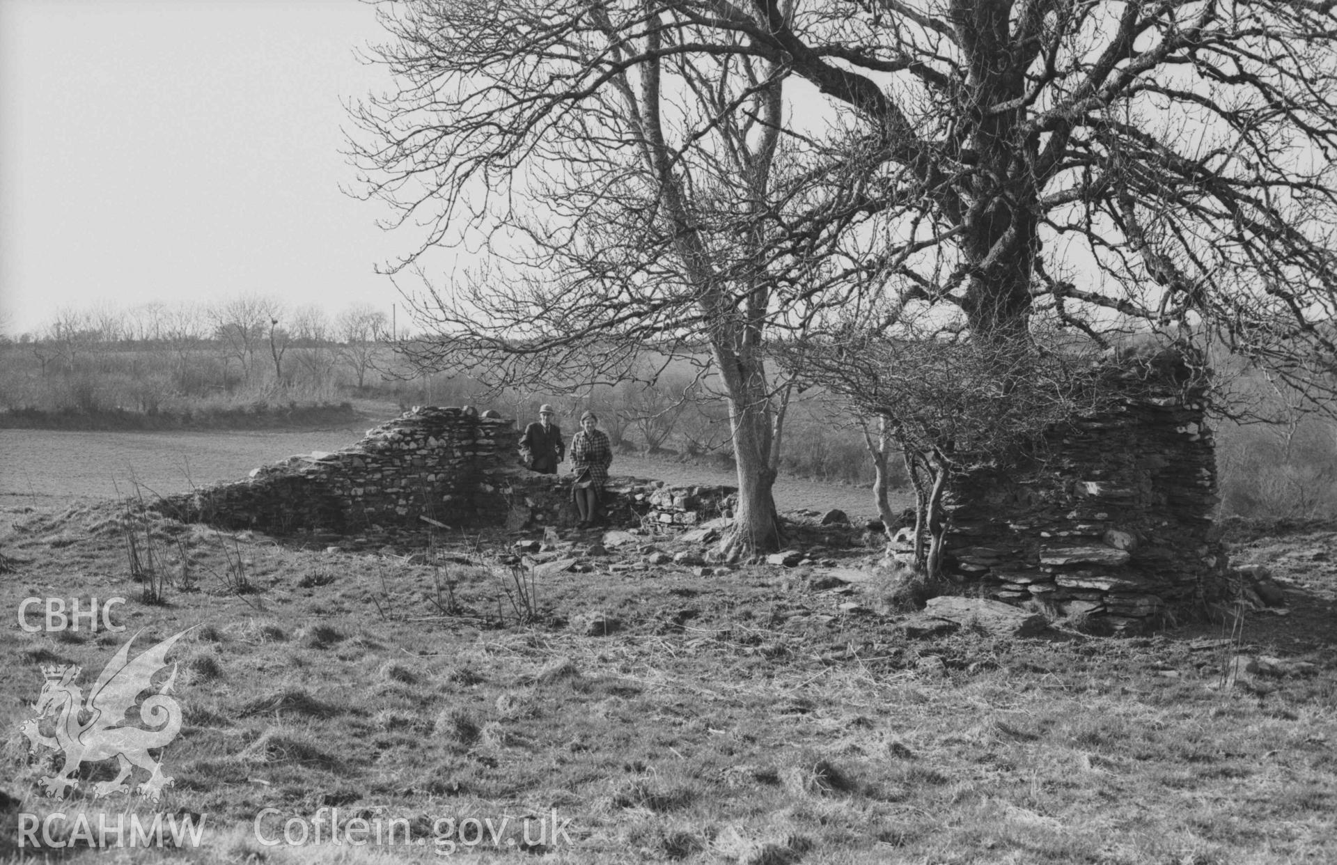 Digital copy of a black and white negative showing two people by the Llanfairtrefhelygen church ruins. Photographed by Arthur Chater on 5 April 1969. Looking north west from Grid Reference SN 3440 4413.