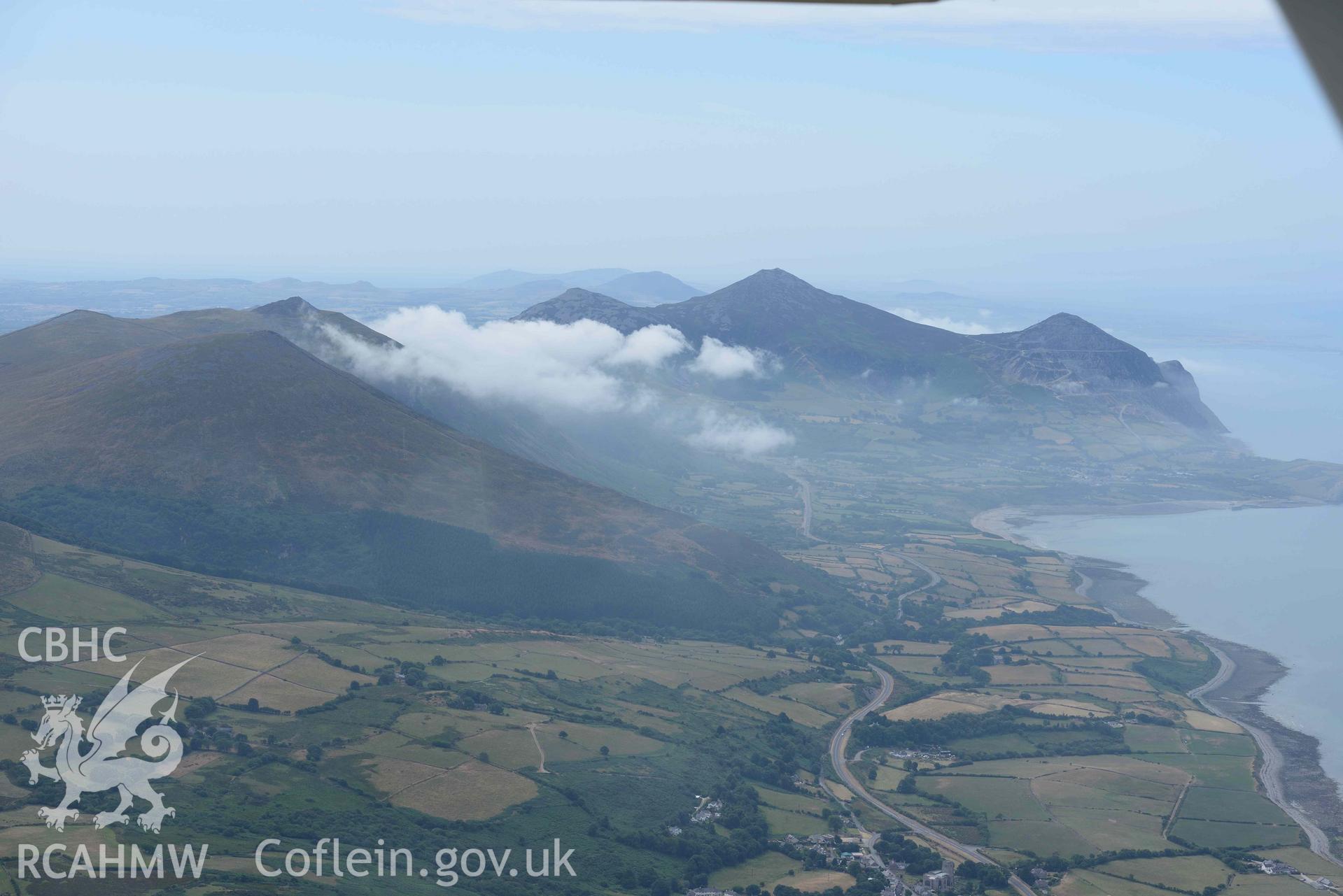 Landscape around Tre'r Ceiri and Clynnog Fawr village. Oblique aerial photograph taken during the Royal Commission’s programme of archaeological aerial reconnaissance by Toby Driver on 10 July 2018.