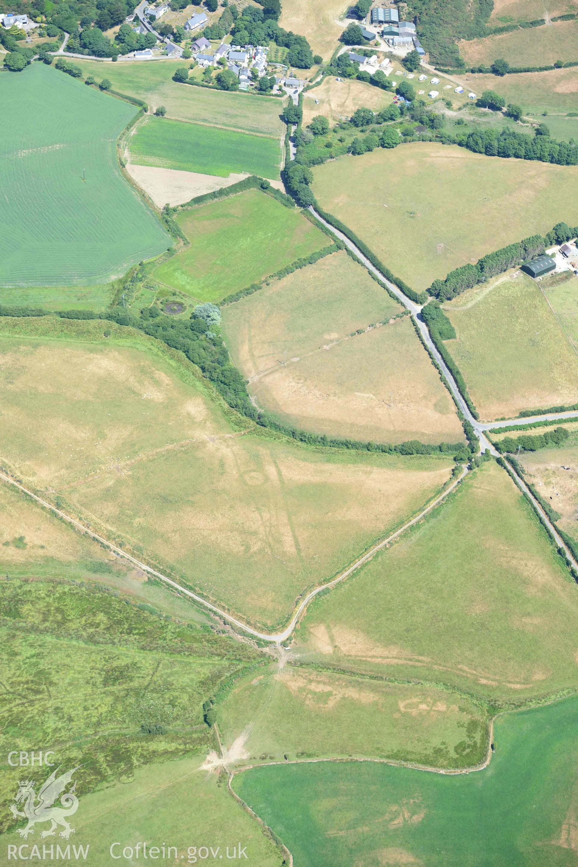 Cropmark complex at Llawr-Dref, and Llangian village beyond. Oblique aerial photograph taken during the Royal Commission’s programme of archaeological aerial reconnaissance by Toby Driver on 10 July 2018.