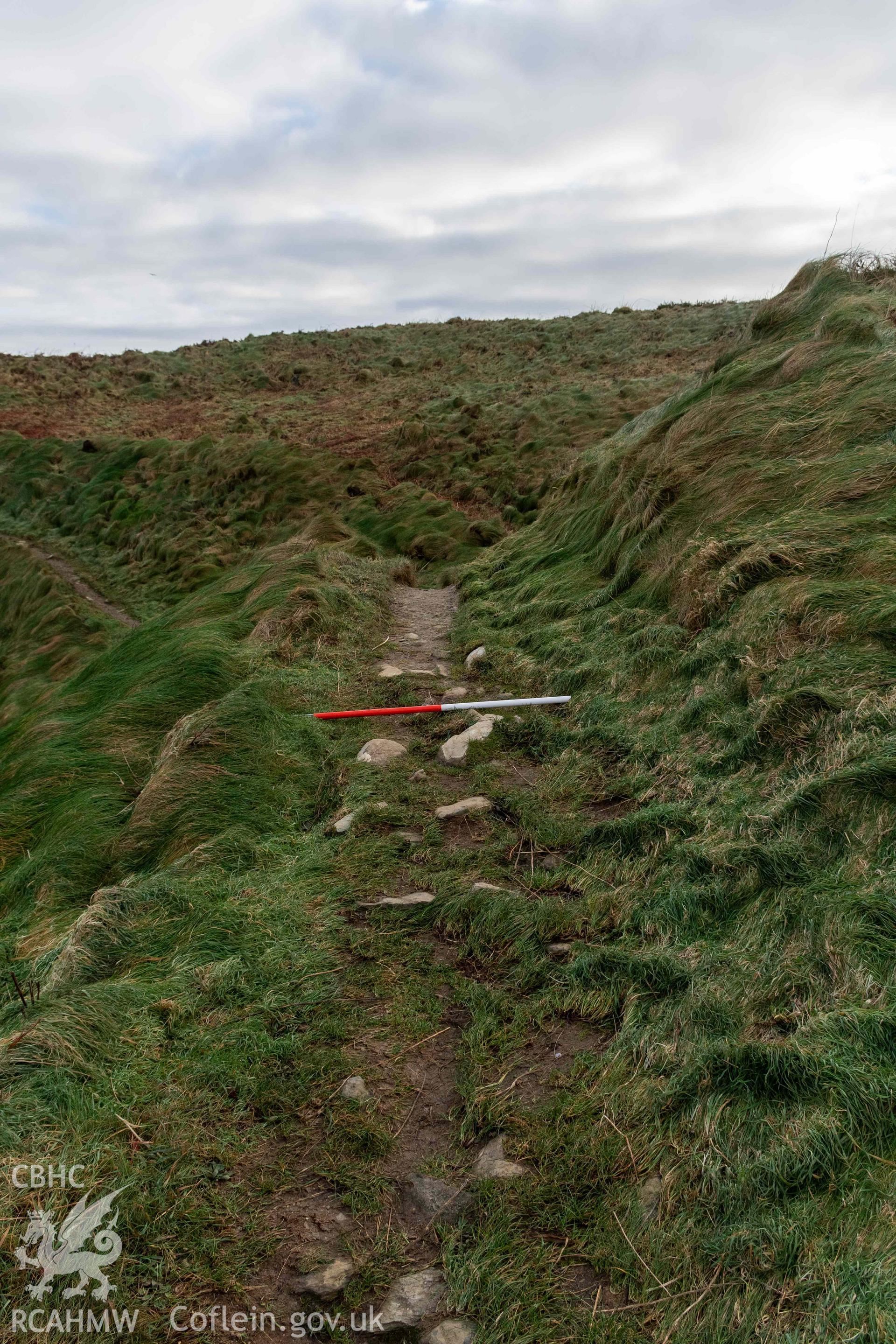 Caer Aber Pwll coastal promontory fort. Exposed rampart walling in footpath running over the inner bank on the eastern side of the fort (with scale).